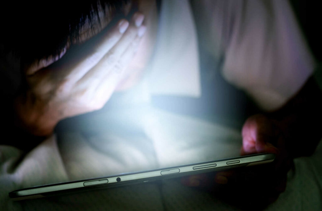 A man holding a digital screen in front of his face while covering his eyes