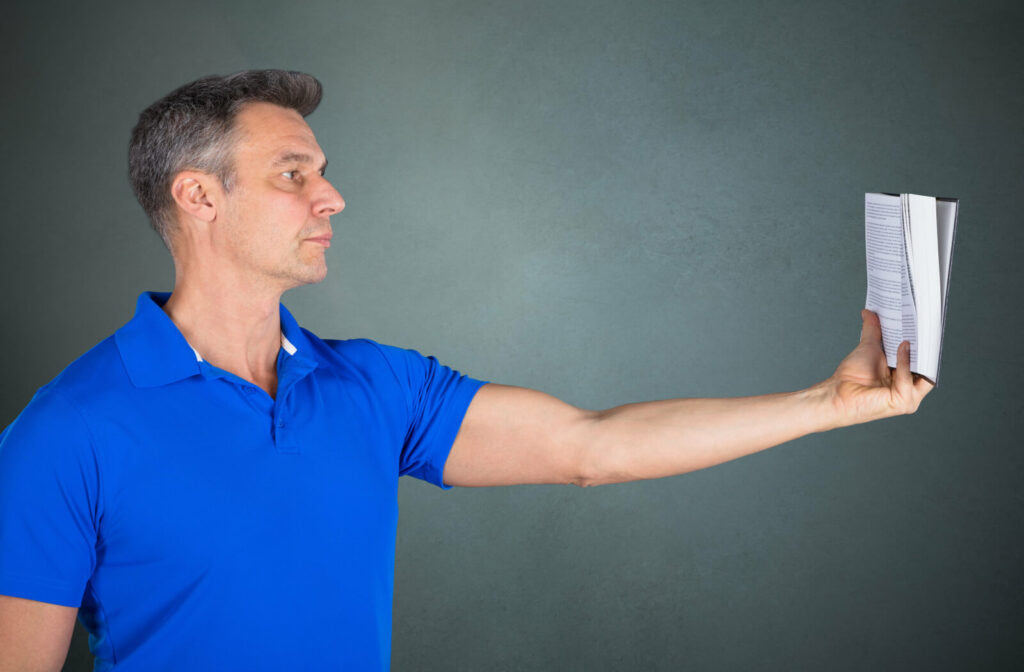 A man in a blue shirt is holding a book a bit far from him while reading it.