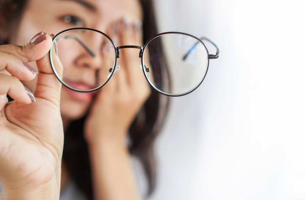 A woman holding a pair of eyeglasses up to her face, as if she is about to put them on.