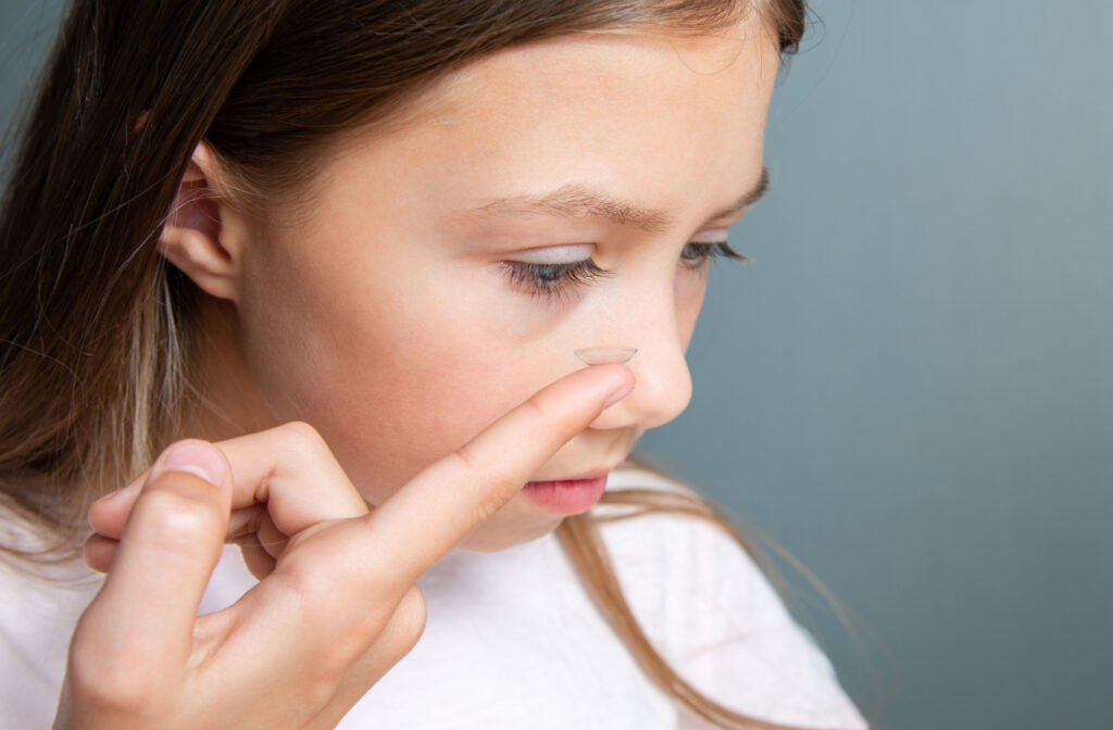 A child putting a contact lens on her right eye using her right hand.