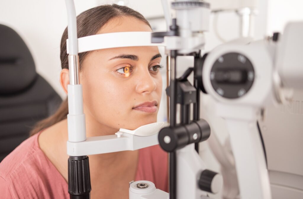A woman during an exam rests her chin on a brace as a slit lamp shines a light in her eye.