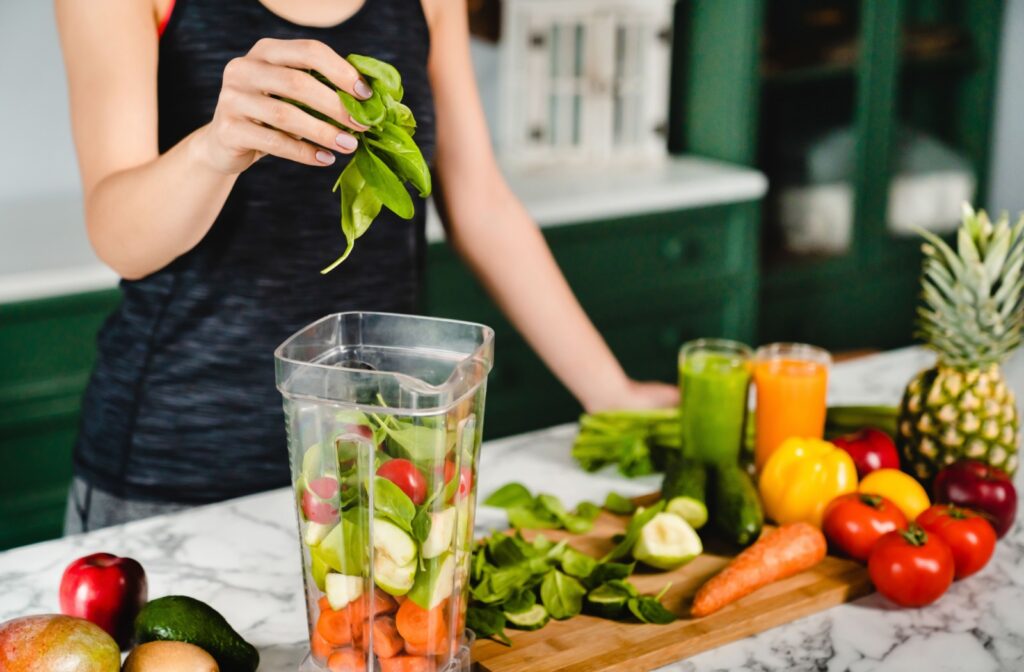 A person puts a handful of leafy greens into a blender next to a cutting board of eye-healthy foods.