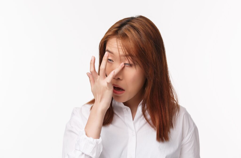 Against a white backdrop, an adult winces as they try to get something out of their eye with their ring finger