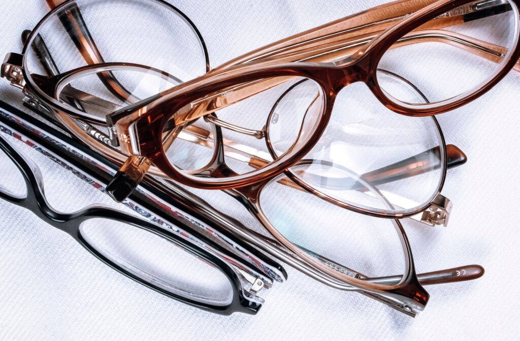 A pile of used prescription glasses in various styles and colors on a white surface.