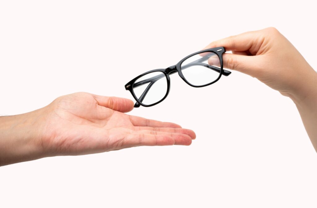 A hand passing a pair of black prescription glasses to another hand