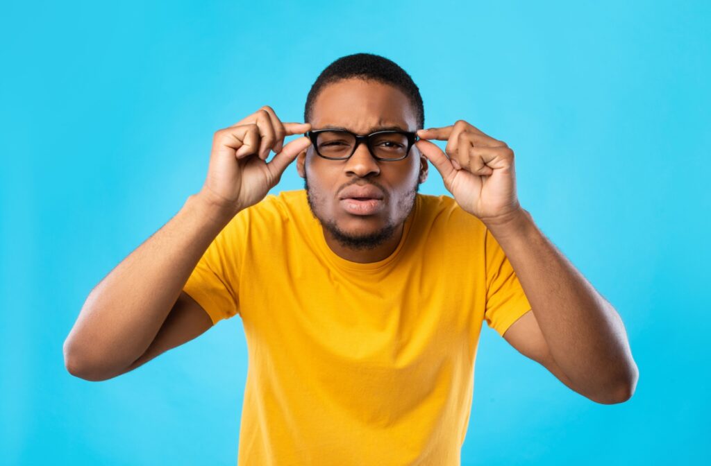 A person holds their glasses as they squint to try to see clearly.