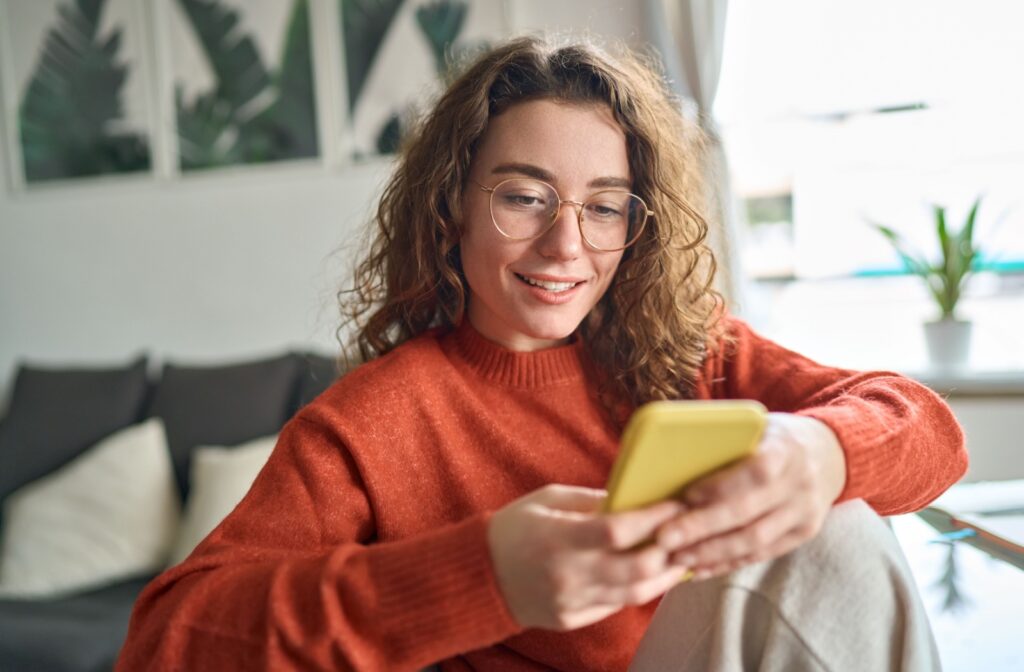A person wearing glasses comfortably reads messages on their phone.