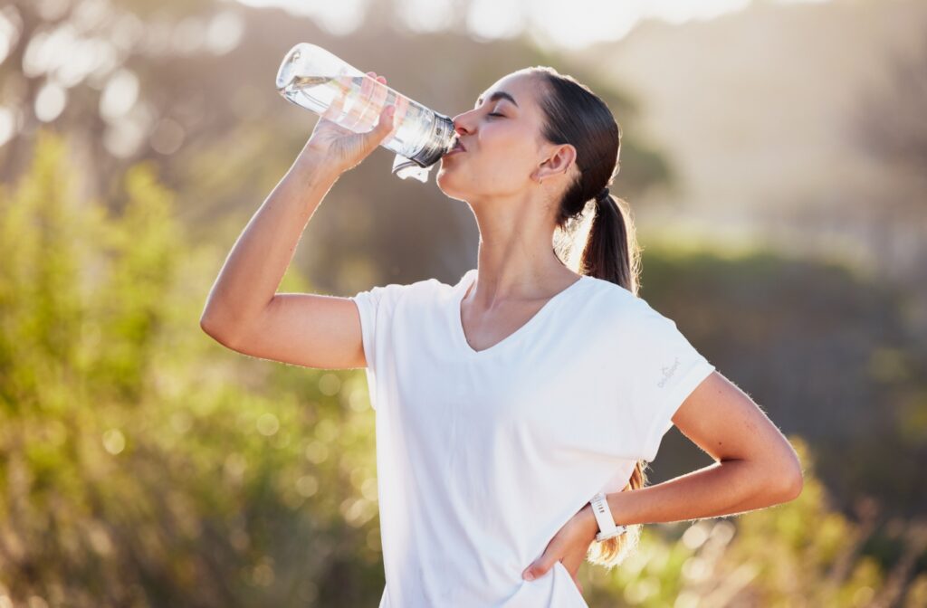 A person drinking from a water bottle outdoors on a sunny day