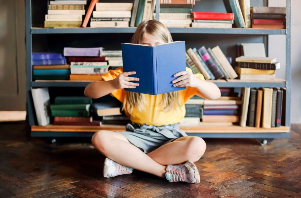 A child sitting in front of a book shelf, reading a book close up.