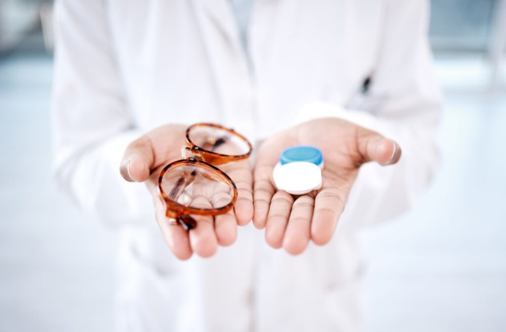 An eye doctor holding glasses in one hand and contact lenses in the other.